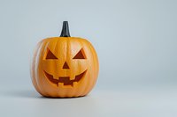 Traditional carved orange pumpkin with classic jack o'lantern face showing happy expression against minimal light gray background with copy space.