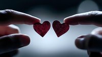 Two red paper hearts held between fingers against backlight creating romantic silhouette. Love concept for Valentine's day cards and relationship themes.