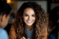 Young mixed race woman with curly hair and bright smile wearing brown cardigan and gray top during casual conversation in cafe setting.