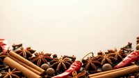 Aromatic winter spices including cinnamon sticks, star anise, allspice berries and dried chili peppers arranged on neutral background for culinary designs.