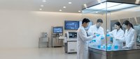 Team of diverse medical professionals in white lab coats collaborating in modern sterile laboratory environment with advanced equipment and monitors.