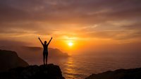 Person silhouette with raised arms celebrating success on cliff overlooking ocean at golden sunset. Achievement motivation freedom concept for wellness.