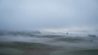 Misty morning landscape with rolling hills covered in fog and low clouds creating atmospheric rural countryside scenery for nature and weather concepts.