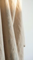 Natural linen fabric drapes hanging in soft folds with warm sunlight creating gentle shadows and highlights on textured beige material for home decor.