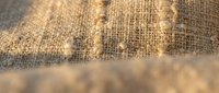 Closeup of natural burlap fabric texture with woven fibers and earthy tones, suitable for backgrounds, textile design, and rustic decor projects.