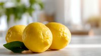 Fresh yellow lemons with green leaf on wooden surface in bright kitchen setting, natural light highlighting citrus texture.
