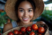 Young Asian woman in straw hat smiling while holding fresh red tomatoes on vine in woven basket, representing healthy lifestyle and local farming.