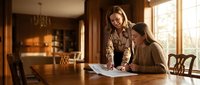 Two professional women collaborating on documents at wooden table in warm office setting with natural lighting for business teamwork presentations.
