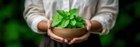 Person holding wooden bowl with fresh green mint leaves against blurred natural background. Organic herbs gardening and sustainable living concept.