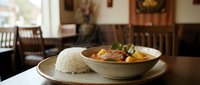 Aromatic curry dish with tender meat and vegetables served alongside fluffy white rice in a ceramic bowl, restaurant dining setting.