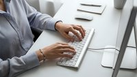 Professional businesswoman typing on white keyboard at modern office desk workspace for productivity and corporate communication tasks.