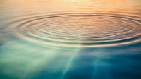 Concentric water ripples spreading across calm surface with golden sunset reflection creating peaceful zen meditation atmosphere for wellness and tranquility concepts.