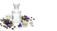 Glass bottle with clear liquid surrounded by purple and white flowers with coffee beans on white background for aromatherapy and natural wellness products.