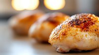 Golden roasted chicken breasts with crispy herb-seasoned skin on white plate, warm kitchen lighting creates cozy dinner atmosphere for culinary content.
