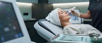 Young woman receiving professional facial treatment at modern beauty clinic with advanced skincare technology equipment for anti-aging therapy.
