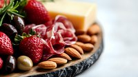 Gourmet charcuterie board with fresh strawberries, cherries, cured meat, cheese, nuts and olives on dark slate platter for entertaining and appetizers.