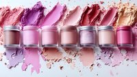 Row of cosmetic powder containers with colorful makeup pigments scattered around in pink, purple, and coral shades for beauty and fashion design.