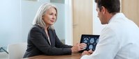Senior Caucasian businesswoman consulting with male doctor about medical scan results on tablet in modern healthcare office setting for professional consultation.