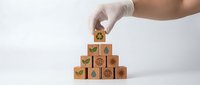 Hand in white glove arranging wooden blocks with environmental sustainability icons into pyramid formation on clean white background.