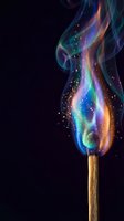 Colorful flame with rainbow spectrum colors rising from wooden match stick against black background with sparkling particles and magical glow effects.
