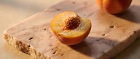 Halved peach with pit exposed on natural stone surface, warm sunlight casting soft shadows, fresh fruit food styling for culinary and recipe content.
