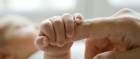 Newborn baby hand grasping adult finger in tender moment showing bond between parent and child. Soft natural lighting captures intimate family connection.