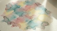 Abstract watercolor paint blends in soft pastel colors creating organic flowing shapes on textured paper surface for artistic backgrounds and creative projects.