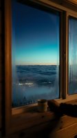Window view of misty mountain valley at dusk with glowing city lights below, wooden frame interior, serene twilight landscape for travel and lifestyle design projects.