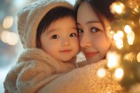 Asian mother and baby daughter share tender moment in warm holiday lighting, wearing cozy winter knits. Gentle bokeh effect creates dreamy atmosphere.