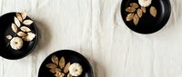 Autumn table setting with white pumpkins and golden leaves in black bowls on cream linen tablecloth for seasonal home decor and holiday dining.