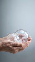 Hand holding transparent soap bubble against neutral gray background, symbolizing fragility, care, protection, and delicate concepts for business and lifestyle applications.