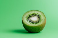 Fresh ripe kiwi fruit half showing detailed seed pattern and vibrant green flesh against minimal green background with soft shadow and copy space.