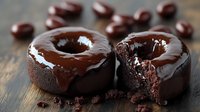 Freshly baked chocolate donuts with glossy ganache glaze and rich fudgy center on rustic wooden surface, one cut to show moist interior texture. Food photography.