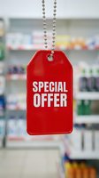 Red special offer price tag hanging on chain in pharmacy store with blurred shelves background, retail sale promotion concept.