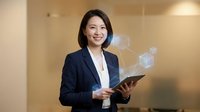 Professional Asian businesswoman holding tablet with digital holographic interface elements in modern office environment for corporate technology presentations.