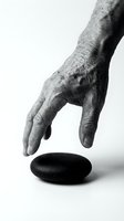 Aged male hand with wrinkled skin reaching toward black stone on white background, isolated for design use, conveying touch, selection, or minimalist concepts.