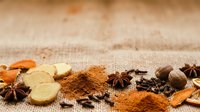 Cinnamon powder, ginger slices, star anise, and nutmeg arranged on burlap fabric for culinary and spice trade themes.