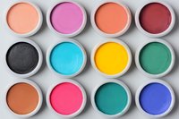 Colorful makeup eyeshadow pigments in round white containers arranged in rows on light gray background. Professional cosmetics palette with vibrant matte shades.