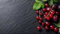 Fresh red currants and cherries with green leaves arranged on dark slate stone background with copy space for food photography and menu design.