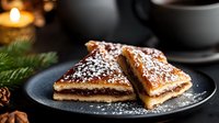 Traditional Christmas strudel slices with apple filling and powdered sugar on dark plate, festive holiday dessert with candle and pine branch decoration.