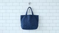 Navy blue canvas tote bag hanging on white subway tile wall. Casual everyday carry bag with sturdy handles for shopping, work or travel accessories.