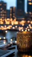 Golden candleholder with ribbed texture glowing against blurred city lights bokeh background creates cozy evening atmosphere on wooden table surface.