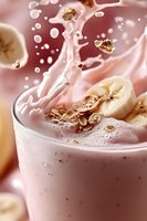 Fresh banana smoothie with milk splash and granola pieces floating in pink glass. Creamy texture with dynamic liquid motion and bubbles creates appetizing drink.