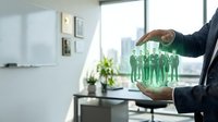 Business professional protecting green human figures with hands in modern office environment representing employee care and team management concepts.