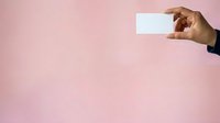Hand holding blank white card against soft pink background, suitable for business cards, promotional materials, and marketing campaigns.