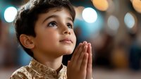 Young boy with hands clasped in prayer, looking up with hope and faith against soft bokeh lights background.