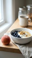 Healthy breakfast bowl with yogurt, blueberries, granola, and banana slices on wooden table by window with fresh apple and coffee mug.
