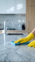 Hand in yellow rubber glove cleaning marble kitchen counter with blue microfiber cloth in modern home interior for housekeeping and hygiene maintenance.