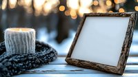 Cozy winter scene with empty rustic wooden photo frame and warm knitted scarf on snowy background with glowing bokeh lights creating magical atmosphere.