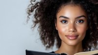 Young African American woman with curly hair smiling while using laptop computer for work or study. Professional portrait for business and technology concepts.